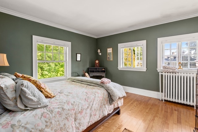 bedroom with radiator, ornamental molding, hardwood / wood-style floors, and multiple windows