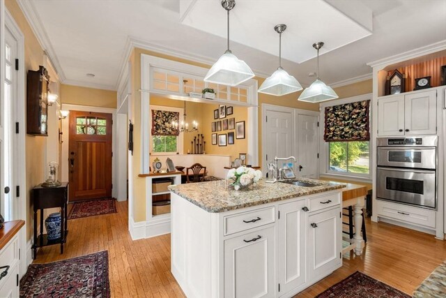 kitchen featuring pendant lighting, light hardwood / wood-style floors, sink, white cabinetry, and stainless steel double oven