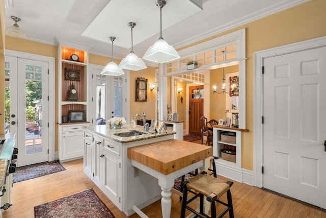 kitchen with light wood-type flooring, light stone counters, sink, white cabinetry, and a center island with sink