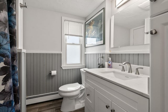 bathroom featuring a baseboard radiator, toilet, wood finished floors, vanity, and wainscoting