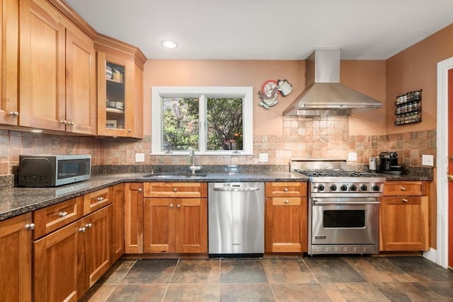 36 Blake Rd, Brookline, MA 02445 - kitchen featuring a sink, wall chimney range hood, dark stone counters, glass insert cabinets, and appliances with stainless steel finishes