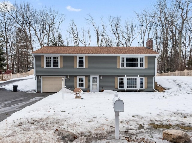 colonial-style house featuring driveway, an attached garage, a chimney, and fence