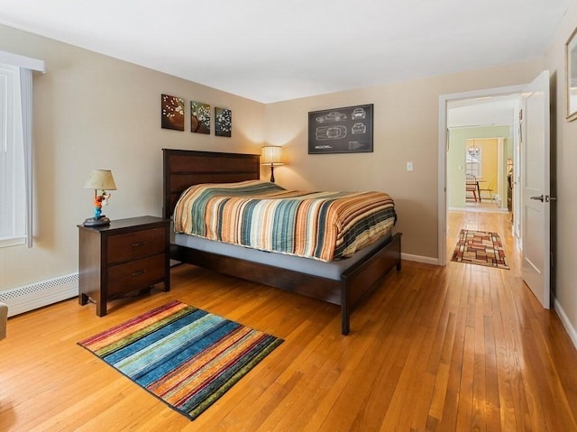 bedroom with a baseboard heating unit, baseboards, and light wood-style floors