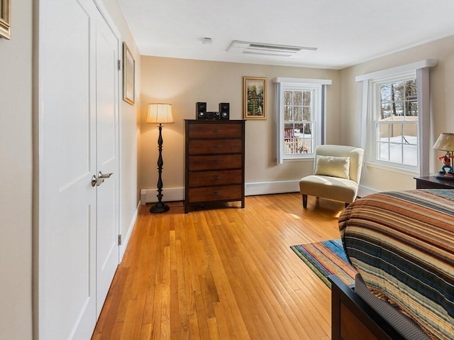 bedroom featuring a baseboard heating unit, light wood-style flooring, visible vents, and baseboards