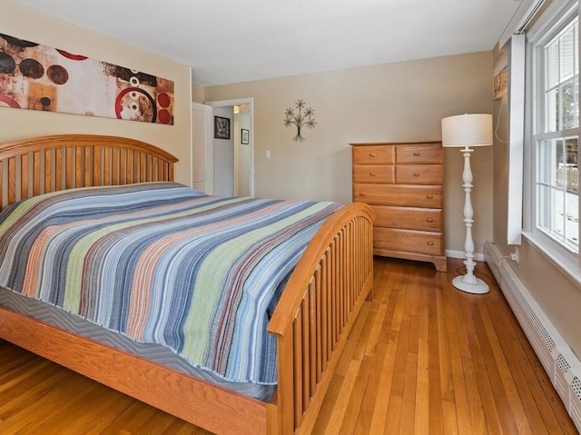 bedroom with multiple windows, light wood finished floors, and baseboard heating