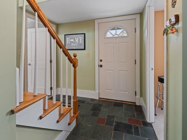 foyer entrance featuring stone finish floor, baseboards, and stairway