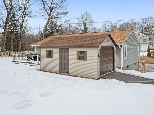 snow covered structure featuring an outbuilding and fence