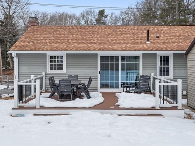 snow covered house featuring roof with shingles and a chimney