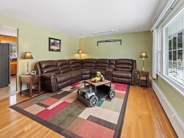 living room with a baseboard radiator, visible vents, baseboards, and wood finished floors