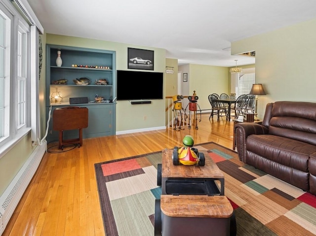 living area with a baseboard heating unit, wood-type flooring, baseboards, and built in features