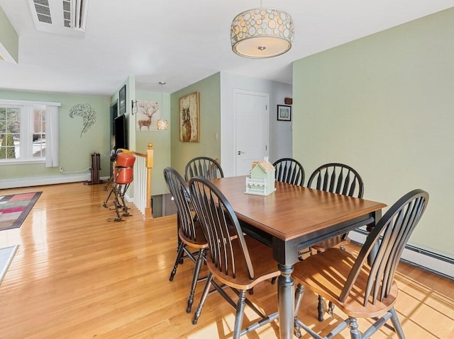 dining room featuring a baseboard radiator, light wood finished floors, baseboards, and visible vents