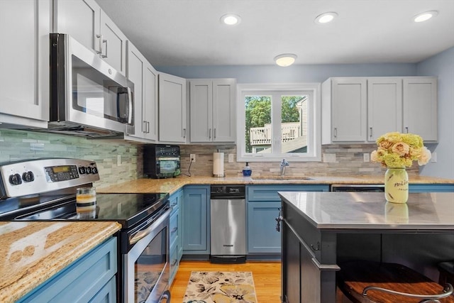31 Monadnock Dr Unit 31, Westford, MA 01886 - kitchen featuring appliances with stainless steel finishes, a sink, blue cabinets, light wood-style floors, and tasteful backsplash