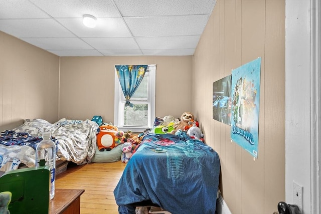 bedroom featuring wood walls, a drop ceiling, and hardwood / wood-style flooring