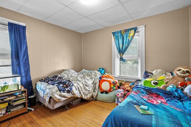 bedroom featuring hardwood / wood-style floors, a paneled ceiling, wood walls, and multiple windows