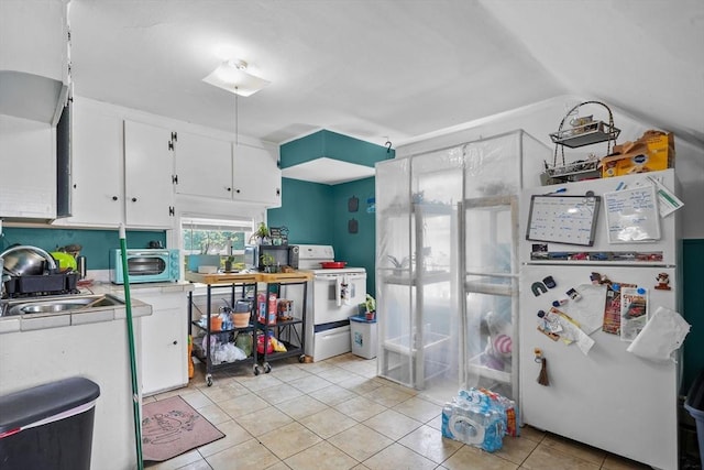 kitchen with white appliances, vaulted ceiling, sink, light tile patterned floors, and white cabinets