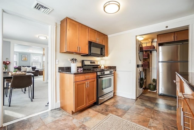 kitchen featuring brown cabinets, visible vents, stainless steel appliances, and stacked washer and clothes dryer