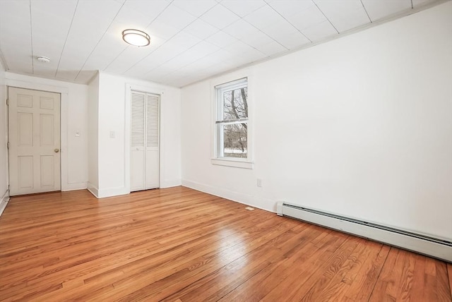 unfurnished bedroom featuring a baseboard radiator, a closet, light wood-style flooring, and baseboards