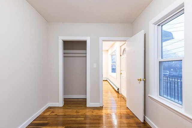 unfurnished bedroom with hardwood / wood-style flooring, multiple windows, and a baseboard heating unit