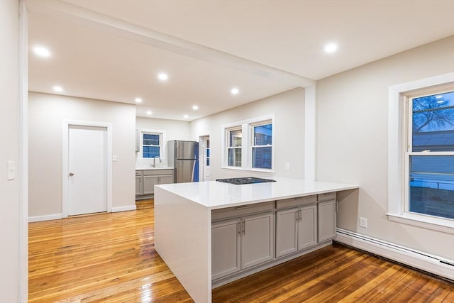 kitchen with stainless steel refrigerator, baseboard heating, kitchen peninsula, light hardwood / wood-style floors, and gray cabinets