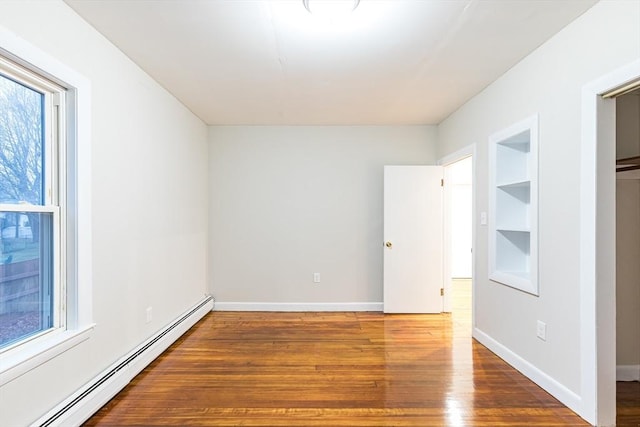 unfurnished bedroom featuring hardwood / wood-style flooring and a baseboard heating unit