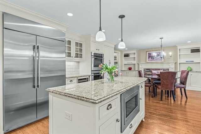 kitchen with built in appliances, light stone counters, white cabinetry, a center island, and light wood-style flooring