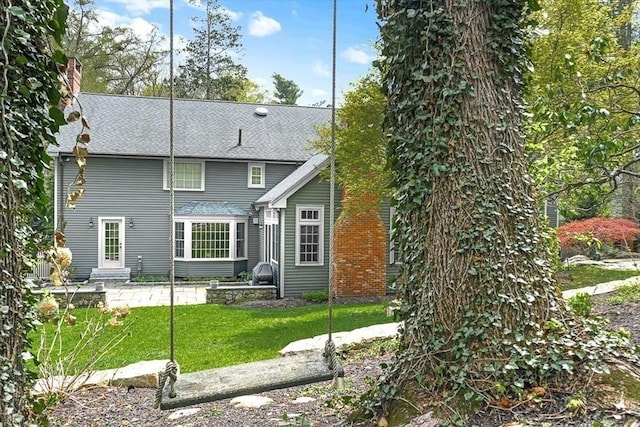 back of house featuring a yard, a chimney, and roof with shingles