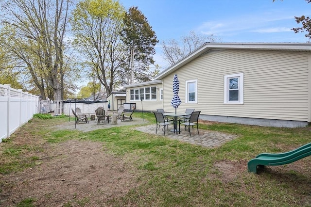 back of house featuring a fenced backyard, a patio area, a playground, a lawn, and a fire pit