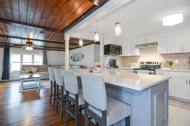 kitchen with white cabinets, a breakfast bar area, stainless steel appliances, backsplash, and under cabinet range hood