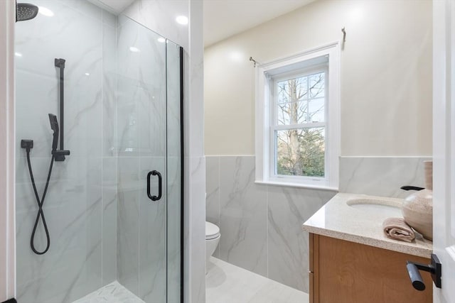 bathroom with vanity, toilet, a shower with shower door, and tile walls