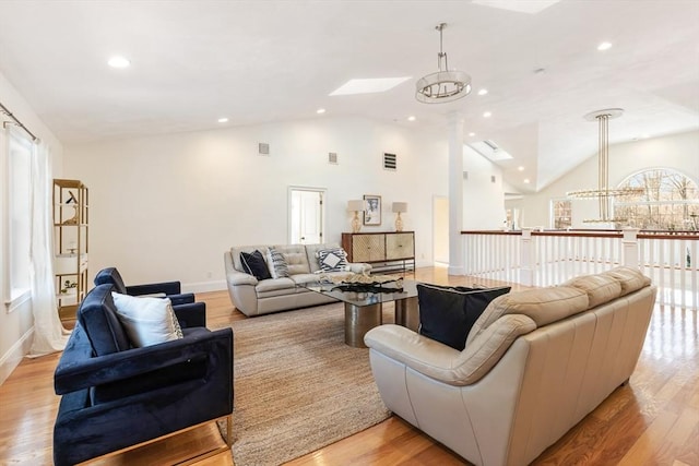 living room featuring light hardwood / wood-style flooring, a skylight, high vaulted ceiling, and a chandelier