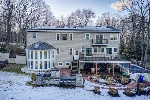 snow covered property with a wooden deck, a sunroom, and solar panels