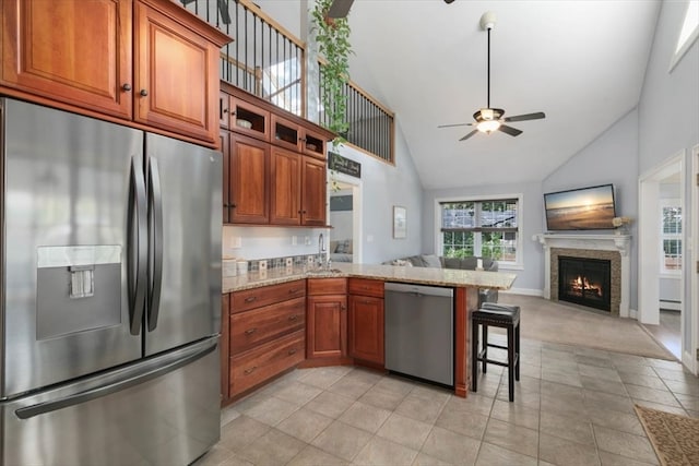 kitchen featuring appliances with stainless steel finishes, light stone counters, high vaulted ceiling, a kitchen bar, and ceiling fan