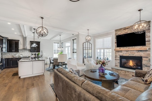 living room featuring wood-type flooring, ornamental molding, beamed ceiling, a stone fireplace, and a notable chandelier