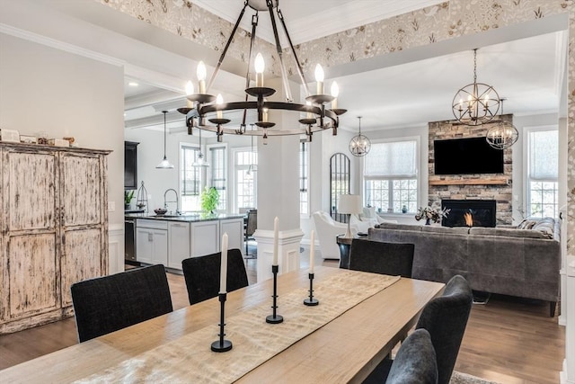 dining room featuring a wealth of natural light, an inviting chandelier, ornamental molding, a stone fireplace, and wood finished floors