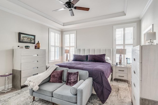 bedroom with ceiling fan, light wood-style flooring, baseboards, ornamental molding, and a tray ceiling