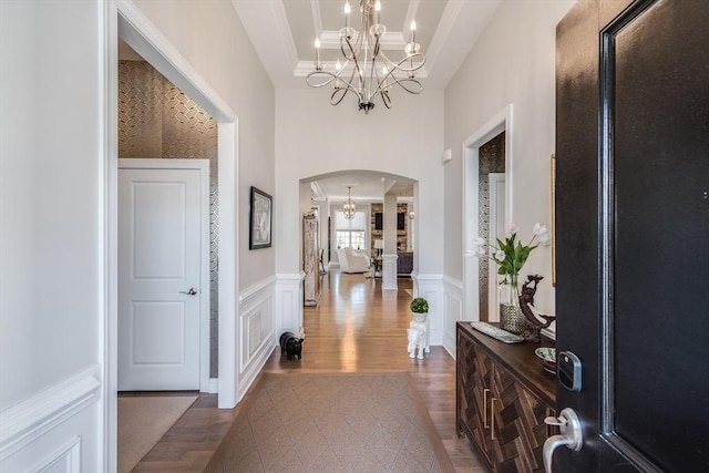 entryway featuring arched walkways, a raised ceiling, wainscoting, a decorative wall, and a notable chandelier