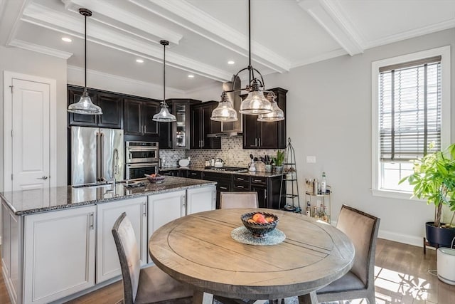 kitchen featuring tasteful backsplash, beamed ceiling, wood finished floors, a kitchen island with sink, and stainless steel appliances