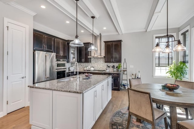 kitchen featuring a sink, light wood-style floors, dark brown cabinets, appliances with stainless steel finishes, and wall chimney exhaust hood