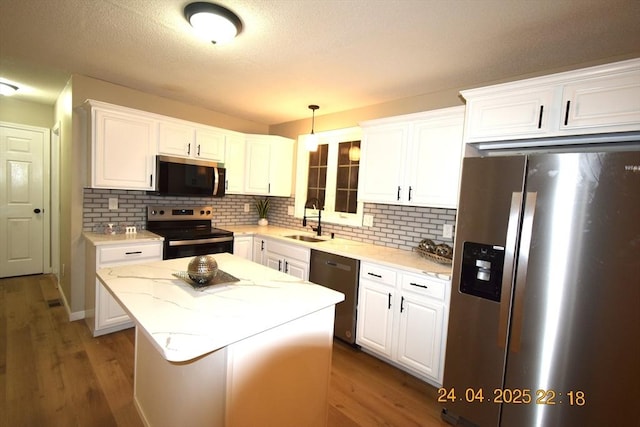 kitchen featuring decorative backsplash, a kitchen island, a sink, white cabinets, and stainless steel appliances