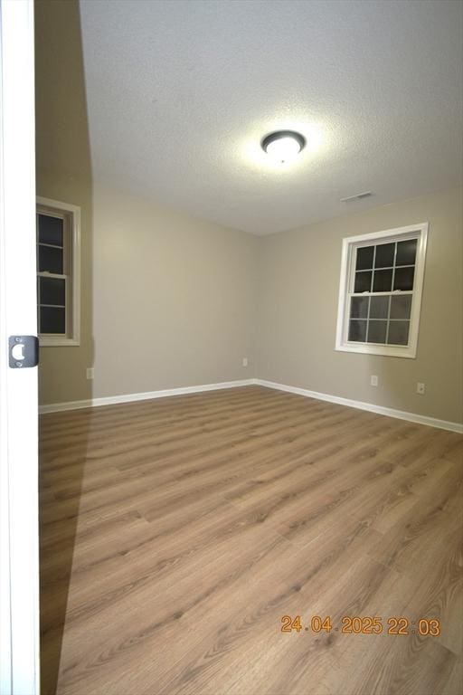 empty room with baseboards, a textured ceiling, and wood finished floors