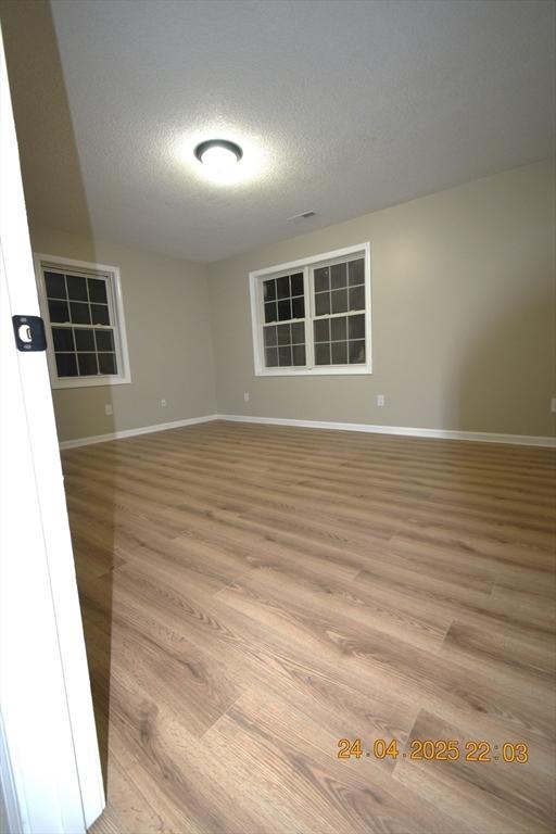 spare room with a textured ceiling, baseboards, and light wood finished floors