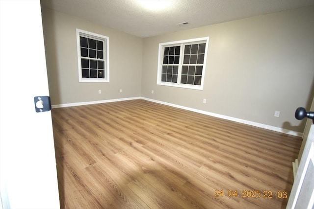 empty room with a textured ceiling, baseboards, and wood finished floors