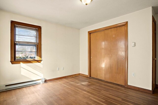 unfurnished bedroom with a baseboard heating unit, baseboards, a closet, and wood finished floors