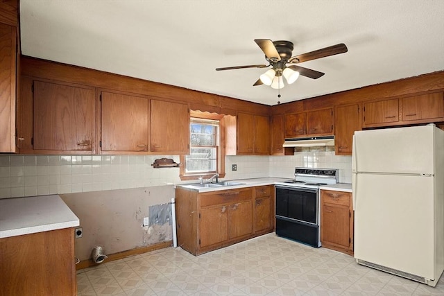 kitchen featuring brown cabinets, electric stove, under cabinet range hood, freestanding refrigerator, and light floors