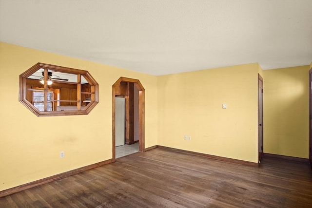 spare room featuring baseboards, arched walkways, and wood finished floors