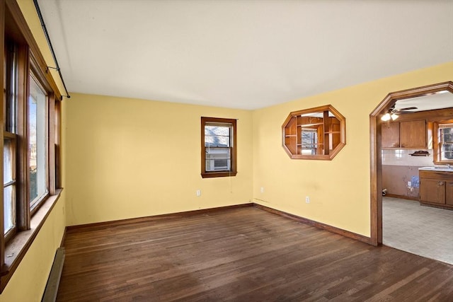 spare room featuring a baseboard heating unit, baseboards, and wood finished floors