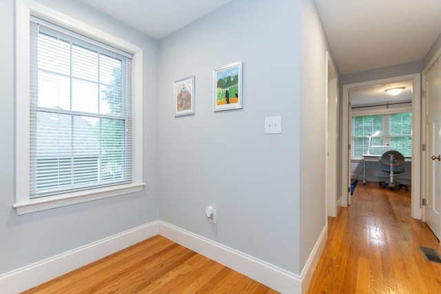 corridor featuring light wood-style flooring, baseboards, and a desk