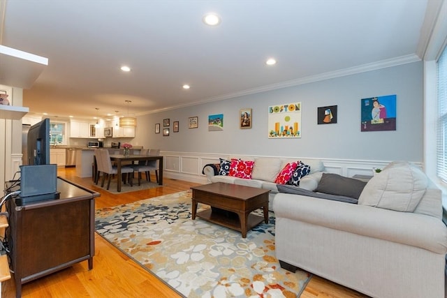living room featuring crown molding, a decorative wall, light wood-style flooring, wainscoting, and recessed lighting
