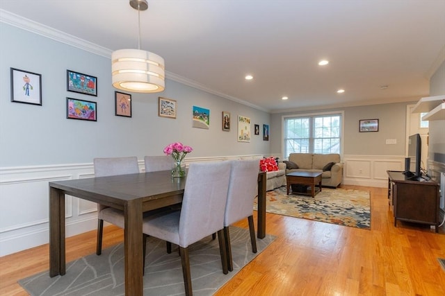 dining area with crown molding, a decorative wall, light wood finished floors, and a wainscoted wall