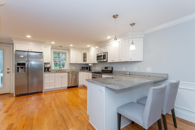 kitchen featuring appliances with stainless steel finishes, a peninsula, ornamental molding, white cabinetry, and a breakfast bar